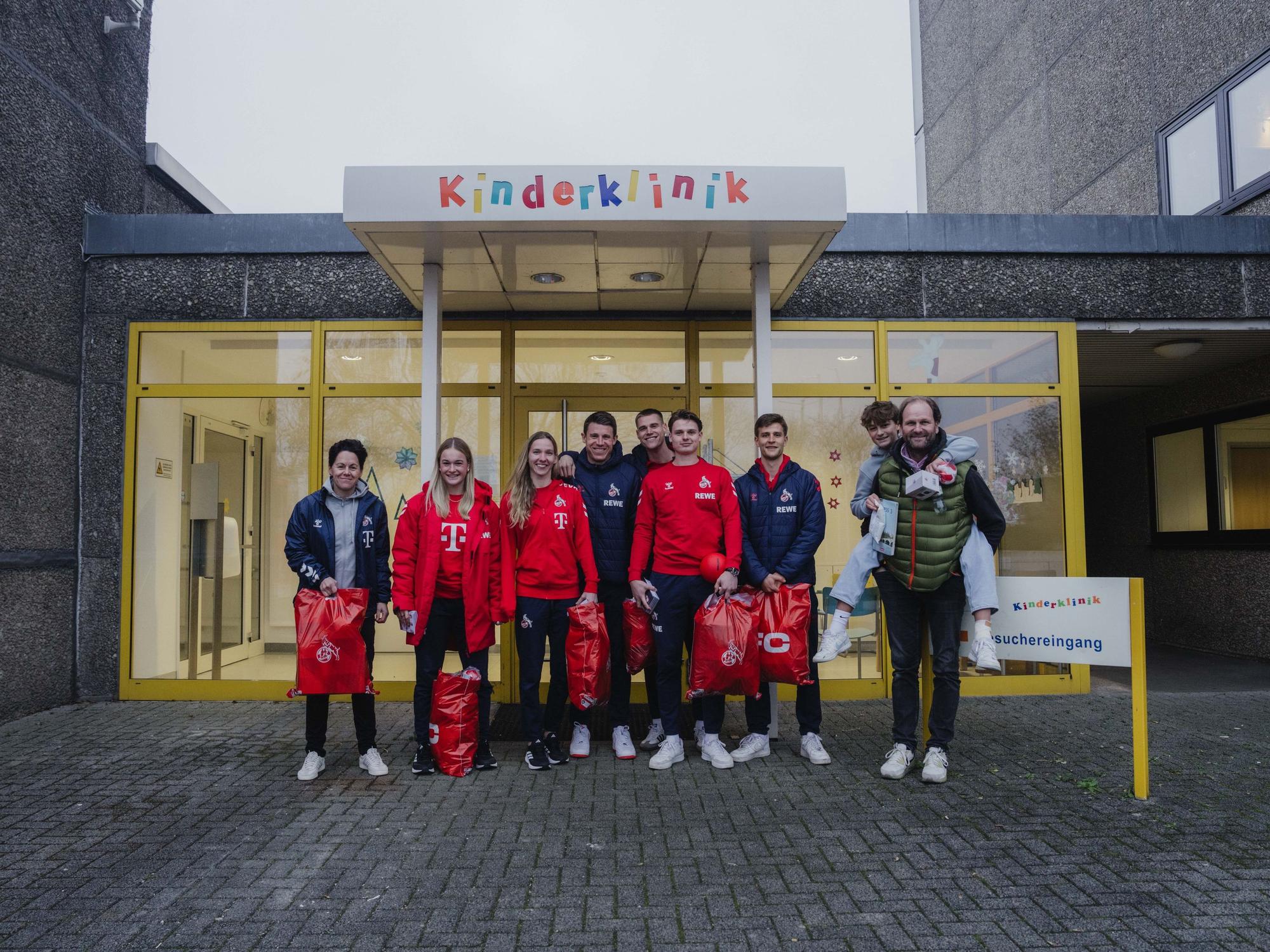 Profis der Männer und Frauen des 1. FC Köln posieren vor dem Eingang der Kinderklinik des Klinikums in Porz.