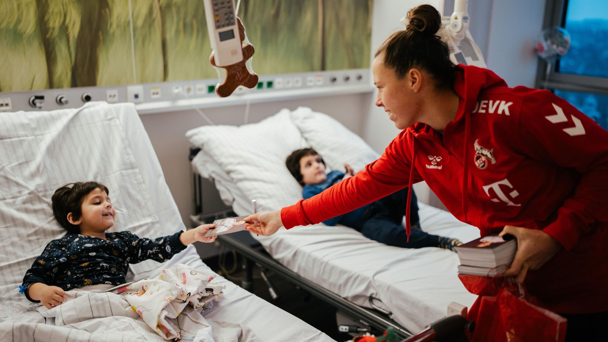 Nicole Billa gibt einem kleinen Kind in einem Krankenhausbett eine Autogrammkarte.