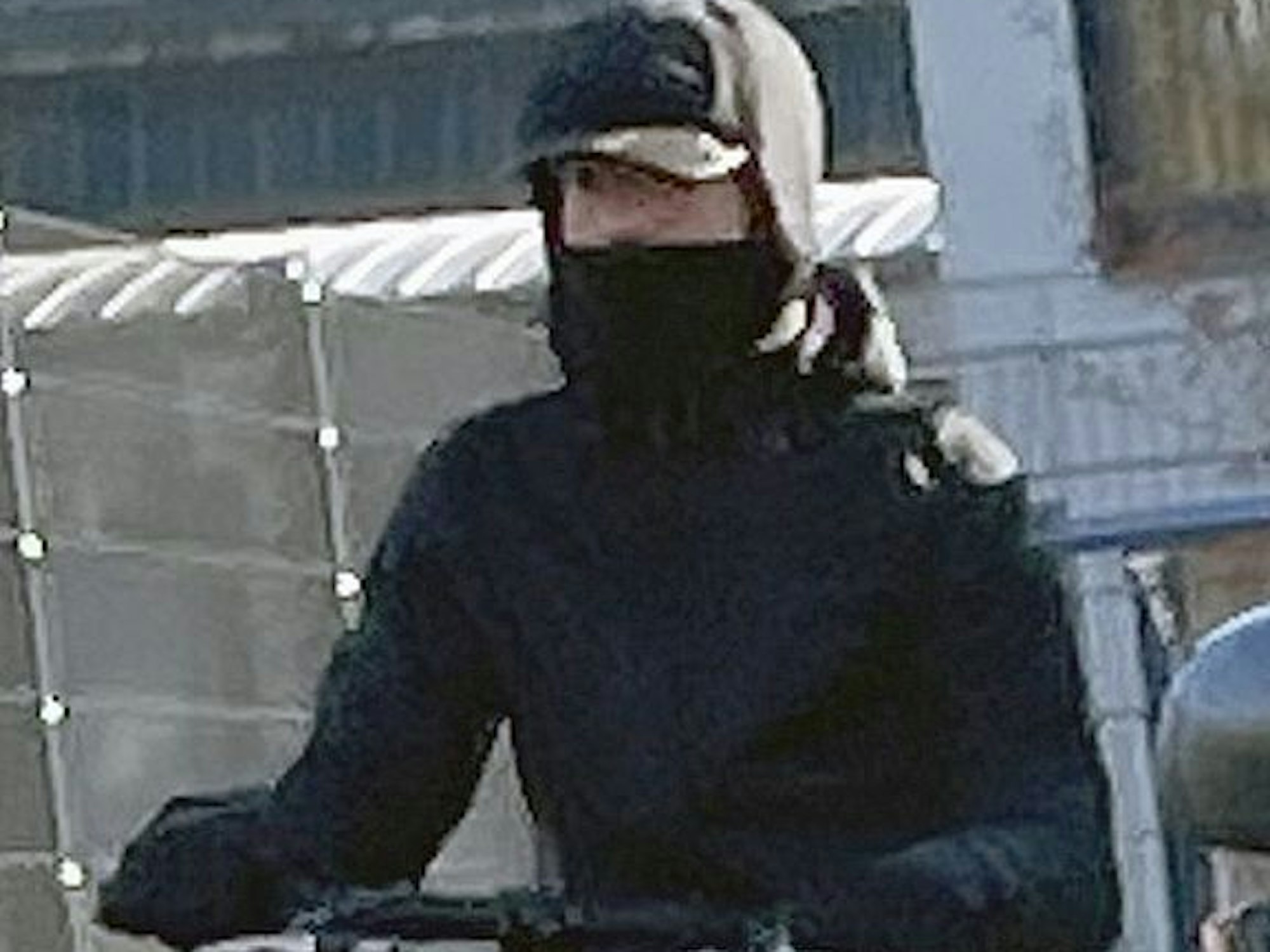 Eine Person hat ein schwarzes Tuch vor dem Mund und eine schwarze Kappe auf dem Kopf.