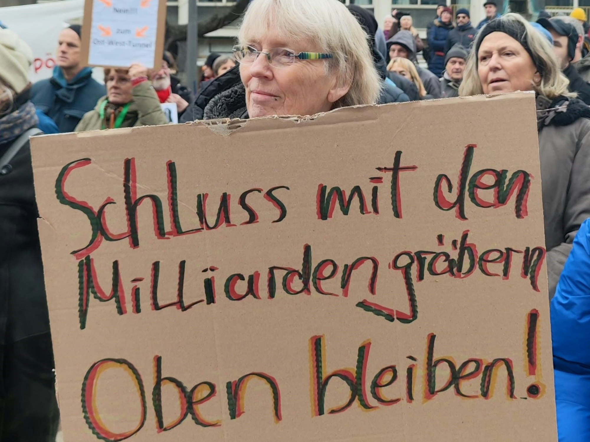 Eine Frau hält ein Pappschild mit der Aufschrift „Schluss mit den Milliardengräbern – oben bleiben!“
