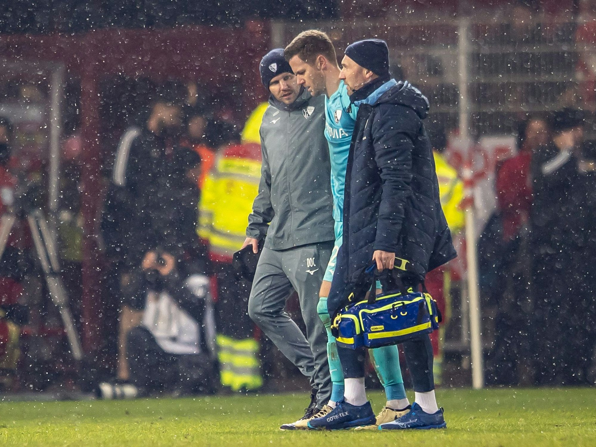 Torwart Patrick Drewes (M.) von VfL Bochum wird vom Platz geführt, nachdem er mit einem Gegenstand am Kopf getroffen wurde.
