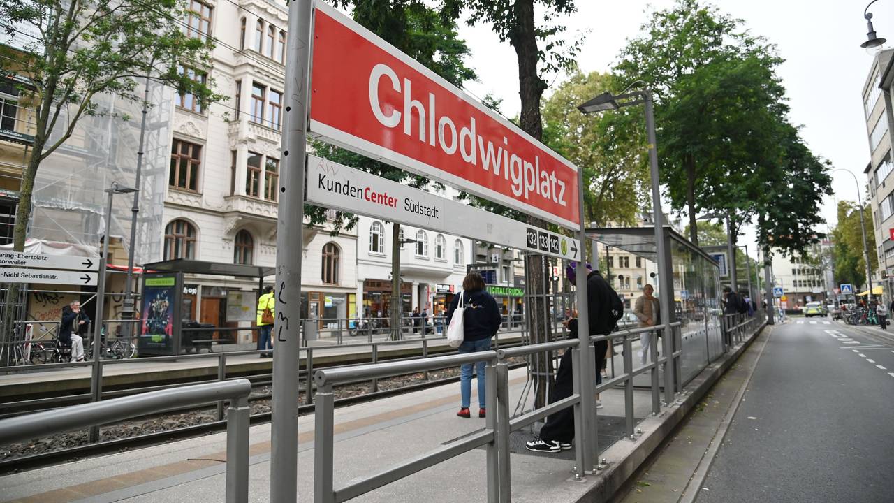 Menschen stehen an einer Straßenbahnhaltestelle in Köln.
