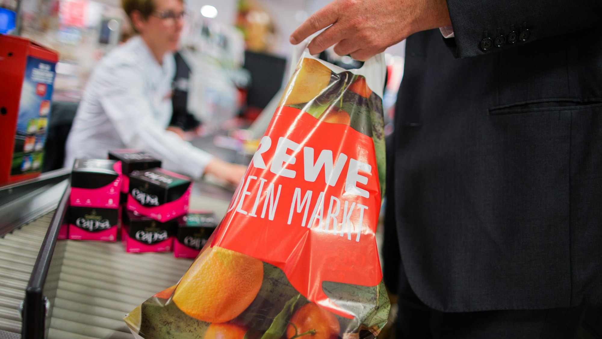 Ein Kunde packt am 31.05.2016 an der Kasse eines Rewe-Marktes in Düsseldorf (Nordrhein-Westfalen) seine Einkäufe in eine Tragetasche aus Plastik. Die Rewe Group möchte eine Reduzierung von Plastikmüll erreichen und verzichtet in Zukunft in ihren Märkten auf Plastiktüten. Foto: Rolf Vennenbernd/dpa ++ +++ dpa-Bildfunk +++
