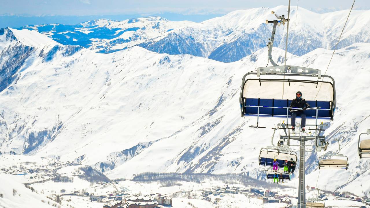 25th january, 2022 - Gudauri, Georgia: skier instructor sit on the char lift and with new Gudauri ski resort and mountains background