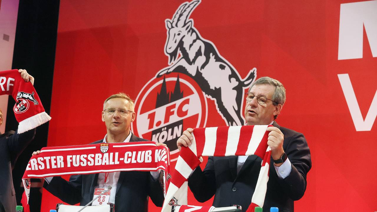 Vize Eckhard Sauren und Präsident Werner Wolf stehen mit FC-Schal auf einem Podium.
