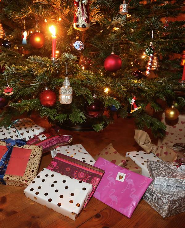 Weihnachtsgeschenke an Heiligabend liegen in einem Wohnzimmer unter einem geschmückten Weihnachtsbaum.