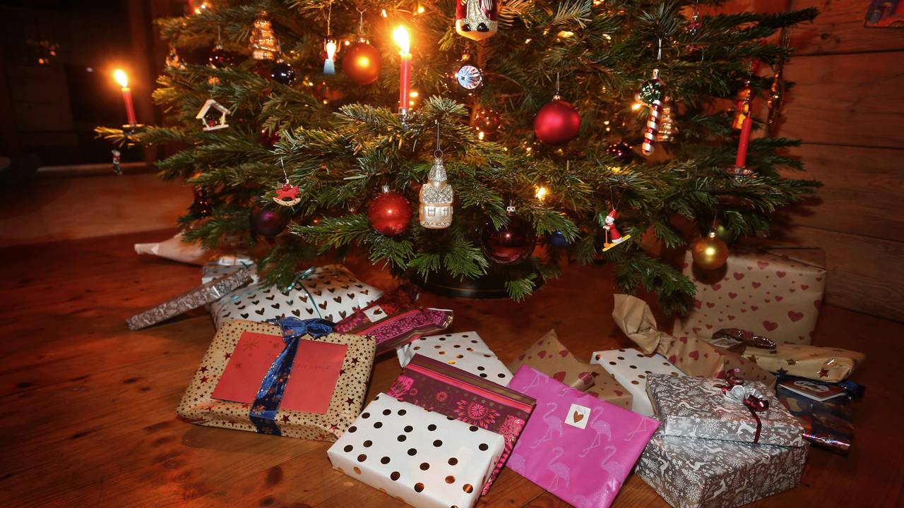Weihnachtsgeschenke an Heiligabend liegen in einem Wohnzimmer unter einem geschmückten Weihnachtsbaum.