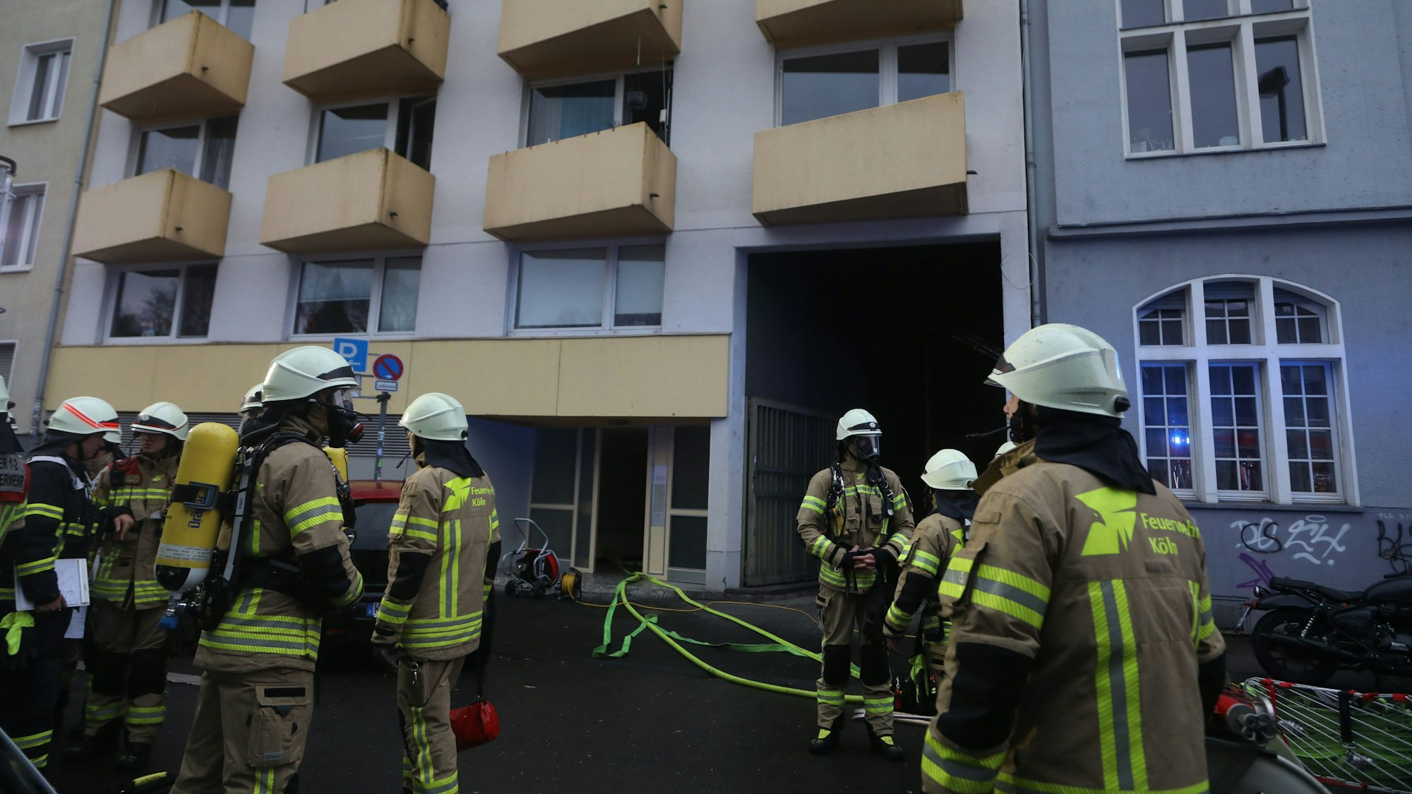 Feuerwehrleute stehen vor einem Mehrfamilienhaus.