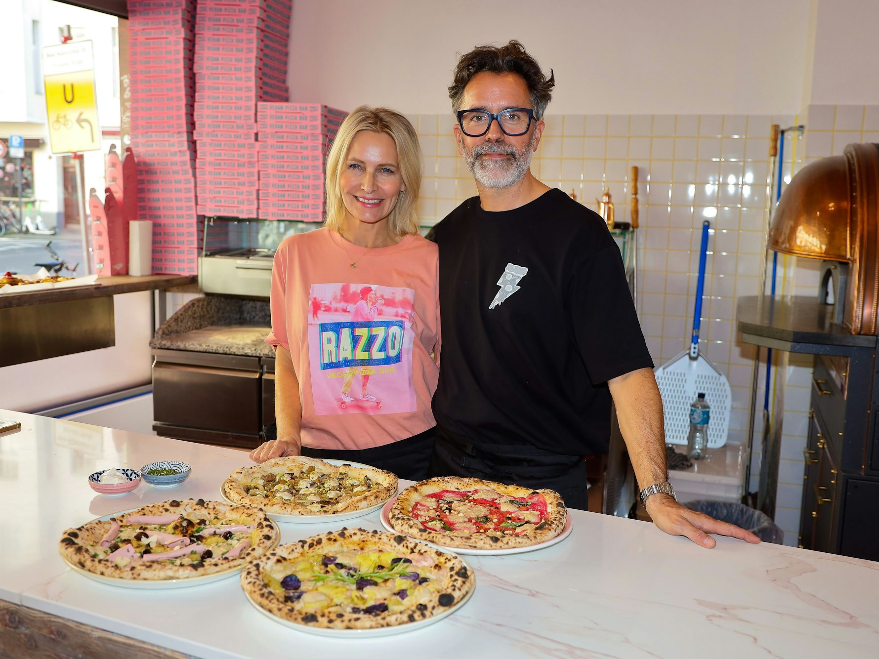 Verena Malta und Ingo Noack stehen an der Theke ihrer Pizzeria, vor ihnen einige vegane Pizzen.