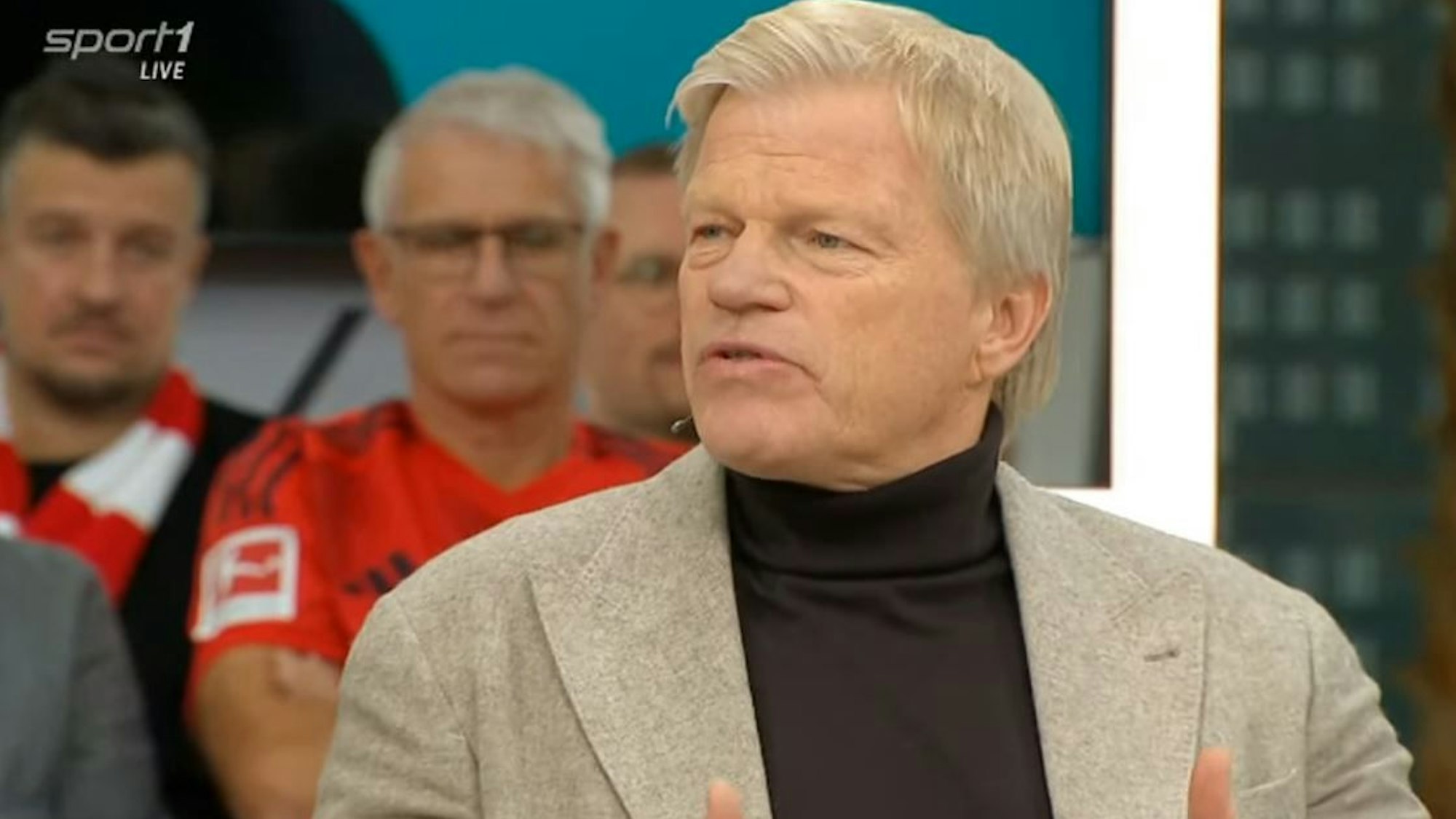 Oliver Kahn sitzt mit Sakko im Doppelpass.