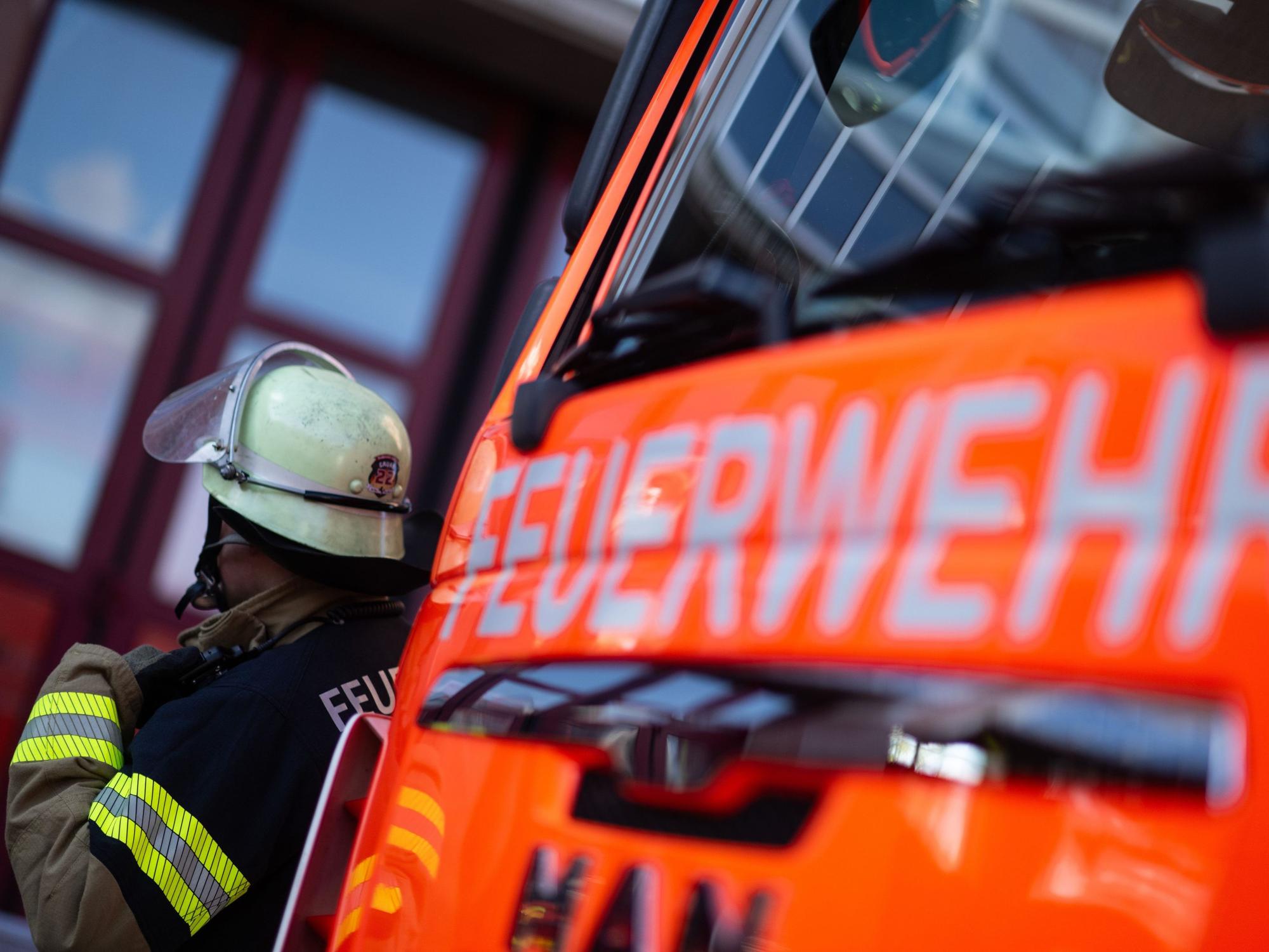 Eine Einsatzkraft der Feuerwehr steht neben einem Einsatzfahrzeug der Feuerwehr.