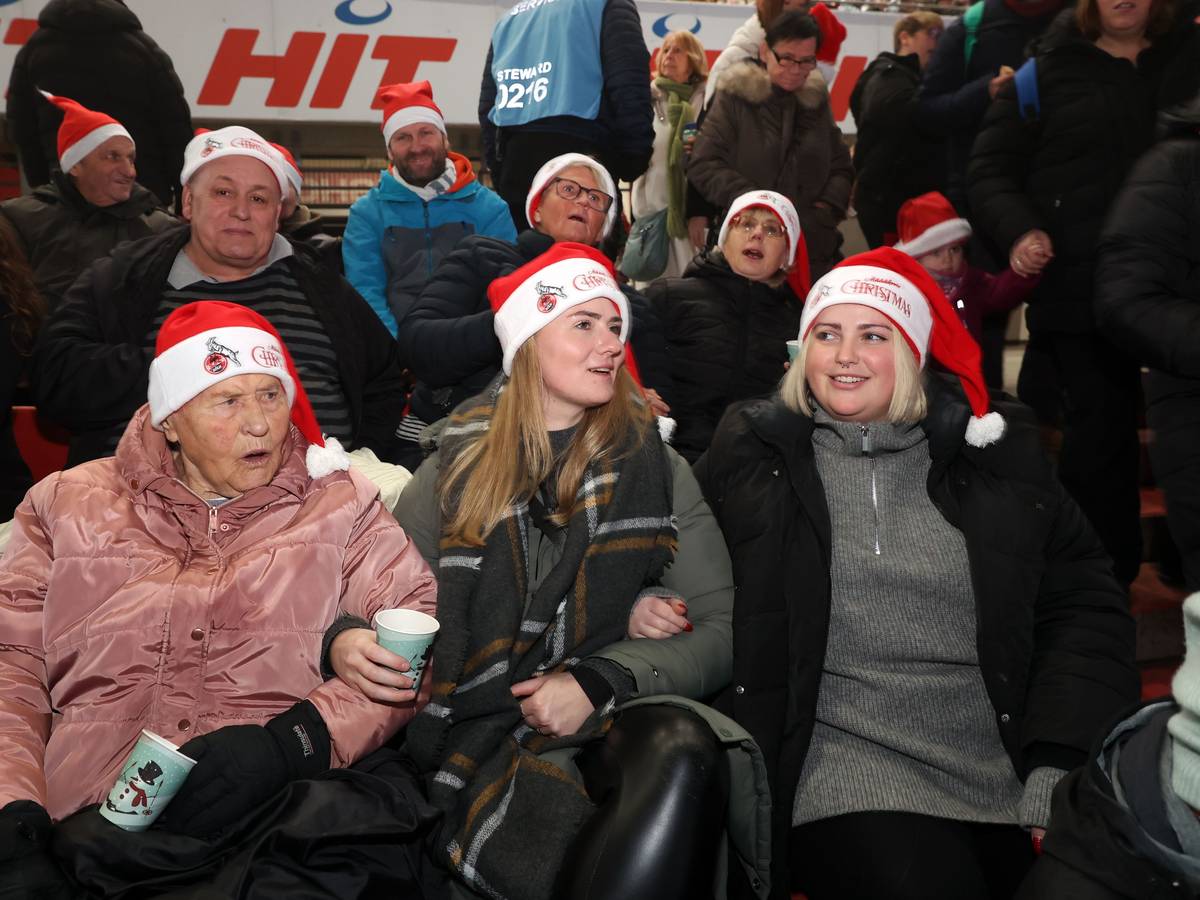Zwei junge Frauen singen mit einer älteren Dame, alle drei tragen Weihnachtsmannmützen.