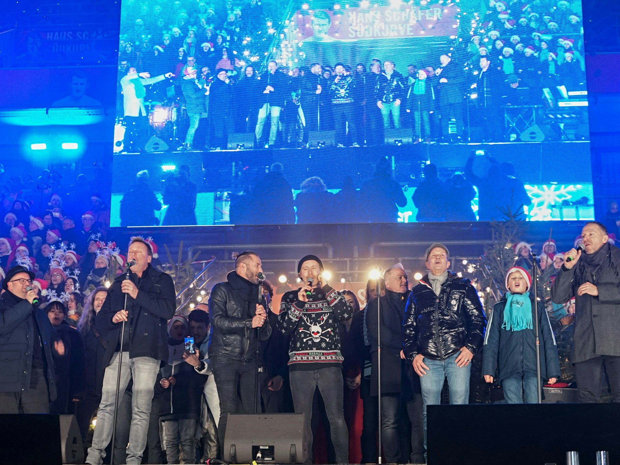 Einige Sängerinnen und Sänger stehen auf der Bühne beim Weihnachtskonzert im Rhein-Energie-Stadion in Köln.