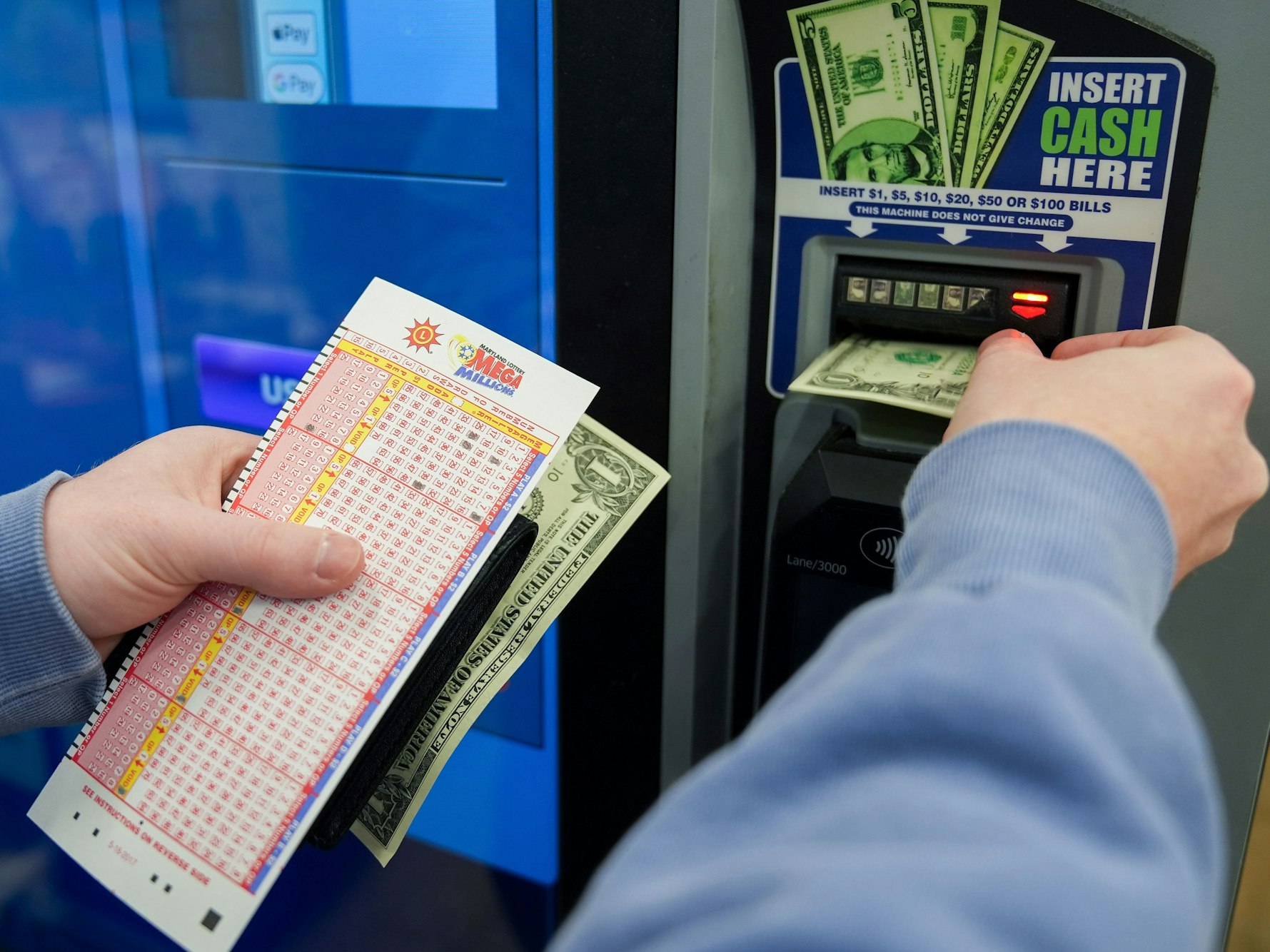 Eine Person wirft Bargeld in ein Selbstbedienungsterminal ein, während sie ihren Spielschein in der Hand hält.