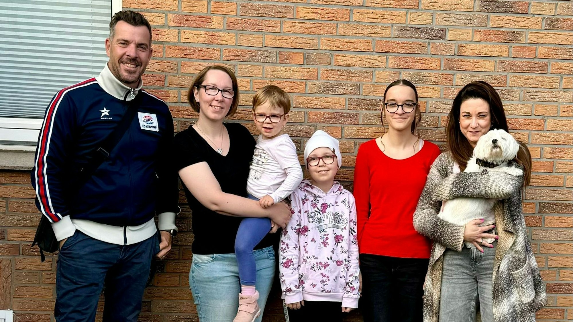 Eine Gruppe posiert für ein Foto vor einer Hauswand.