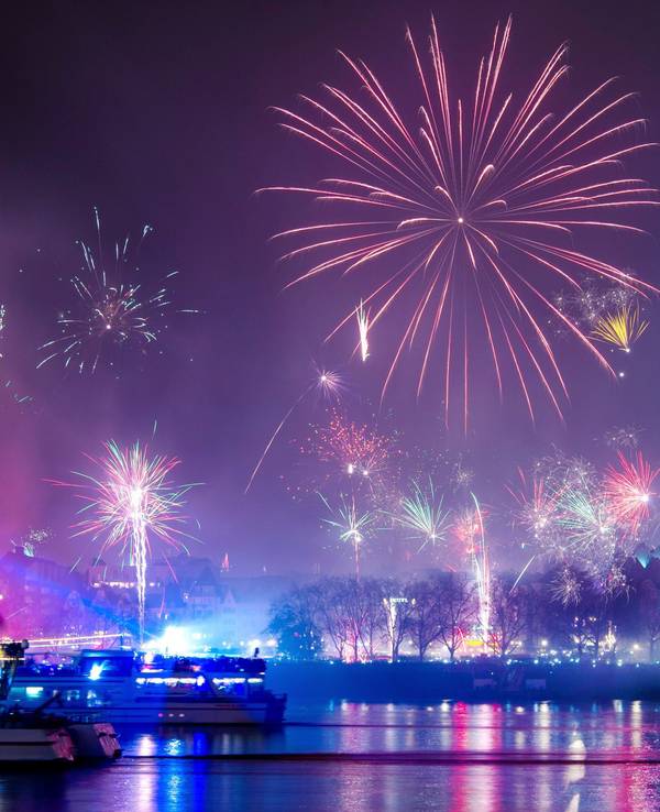 Silvesterraketen explodieren über dem Rhein, im Hintergrund der beleuchtete Dom.