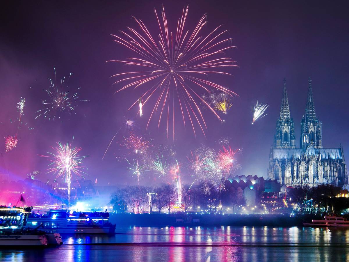 Silvesterraketen explodieren über dem Rhein, im Hintergrund der beleuchtete Dom.