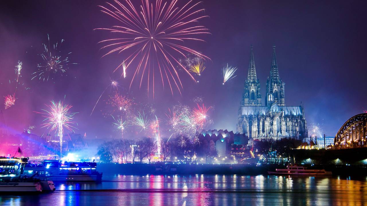 Silvesterraketen explodieren über dem Rhein, im Hintergrund der beleuchtete Dom.