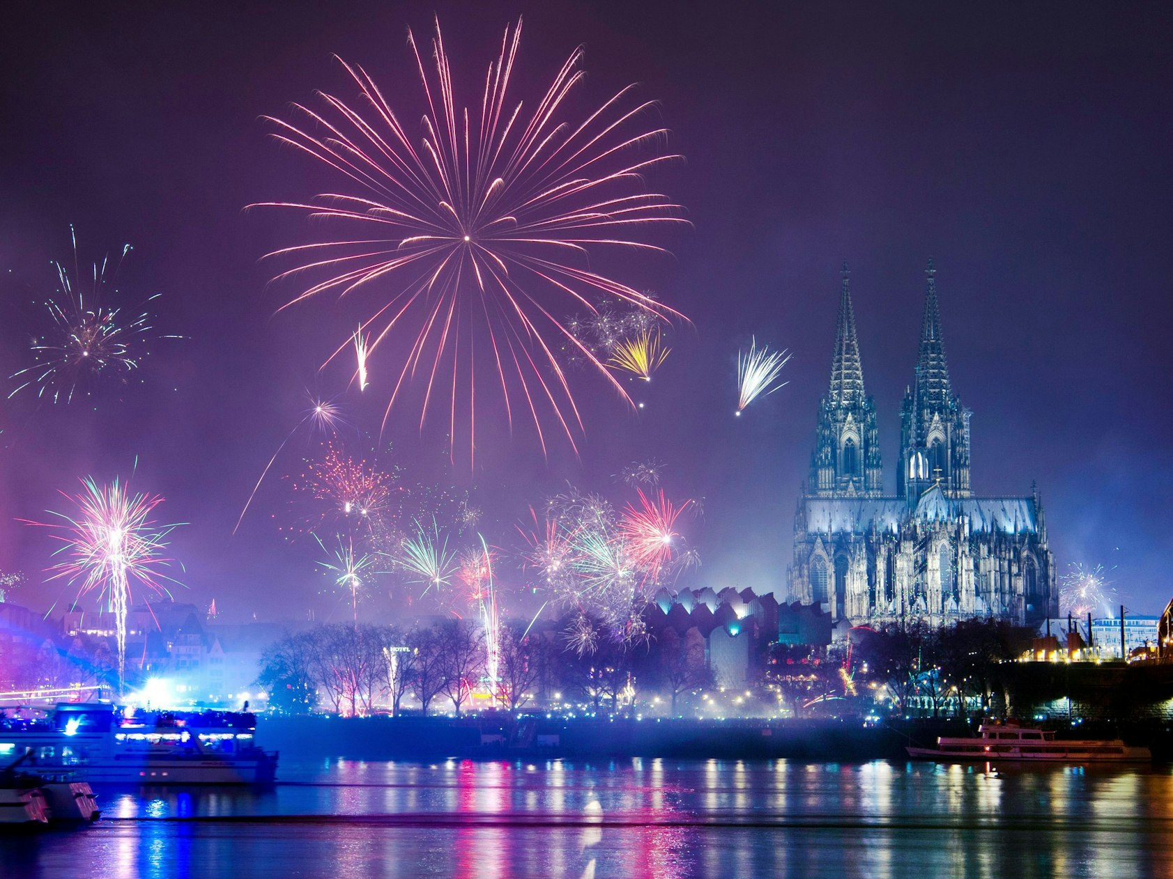 Silvesterraketen explodieren über dem Rhein, im Hintergrund der beleuchtete Dom.