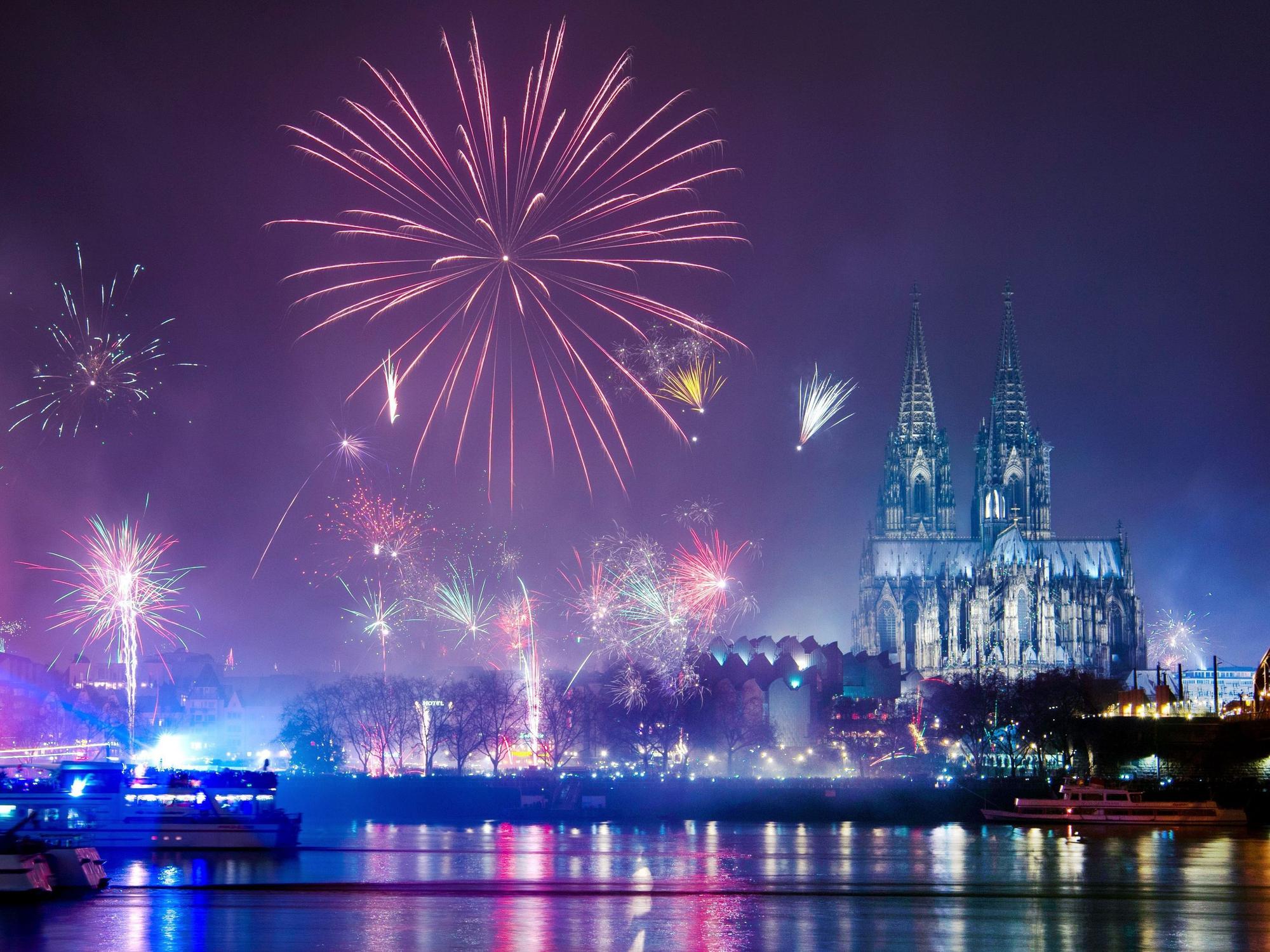Silvesterraketen explodieren über dem Rhein, im Hintergrund der beleuchtete Dom.