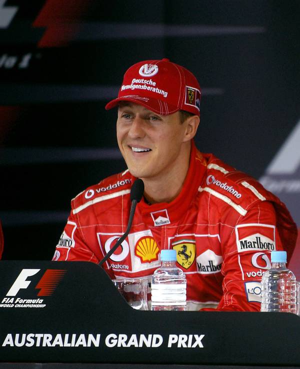 Michael Schumacher lächelt bei einer Pressekonferenz, Juan Pablo Montoya sietzt gelangweilt daneben.