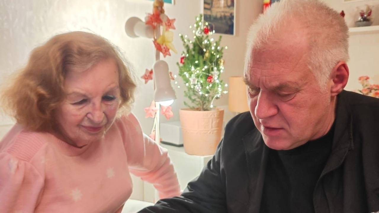 Ein Mann hält ein Schreiben in der Hand, neben ihm sitzt eine ältere Dame am Tisch.