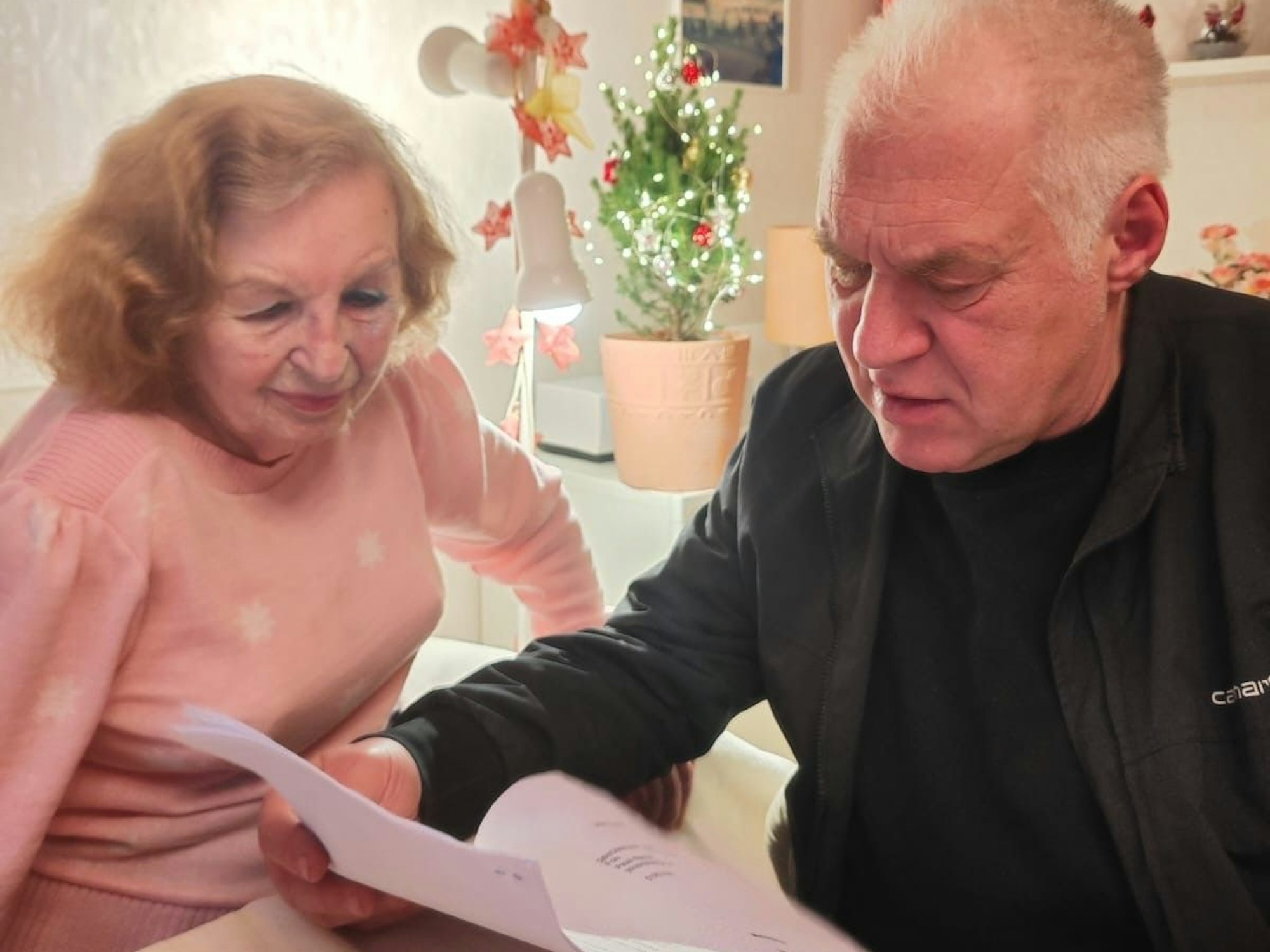 Ein Mann hält ein Schreiben in der Hand, neben ihm sitzt eine ältere Dame am Tisch.