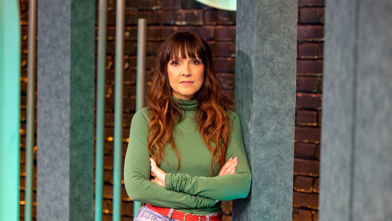 Carolin Kebekus lehnt mit verschränkten Armen an eienr Wand.