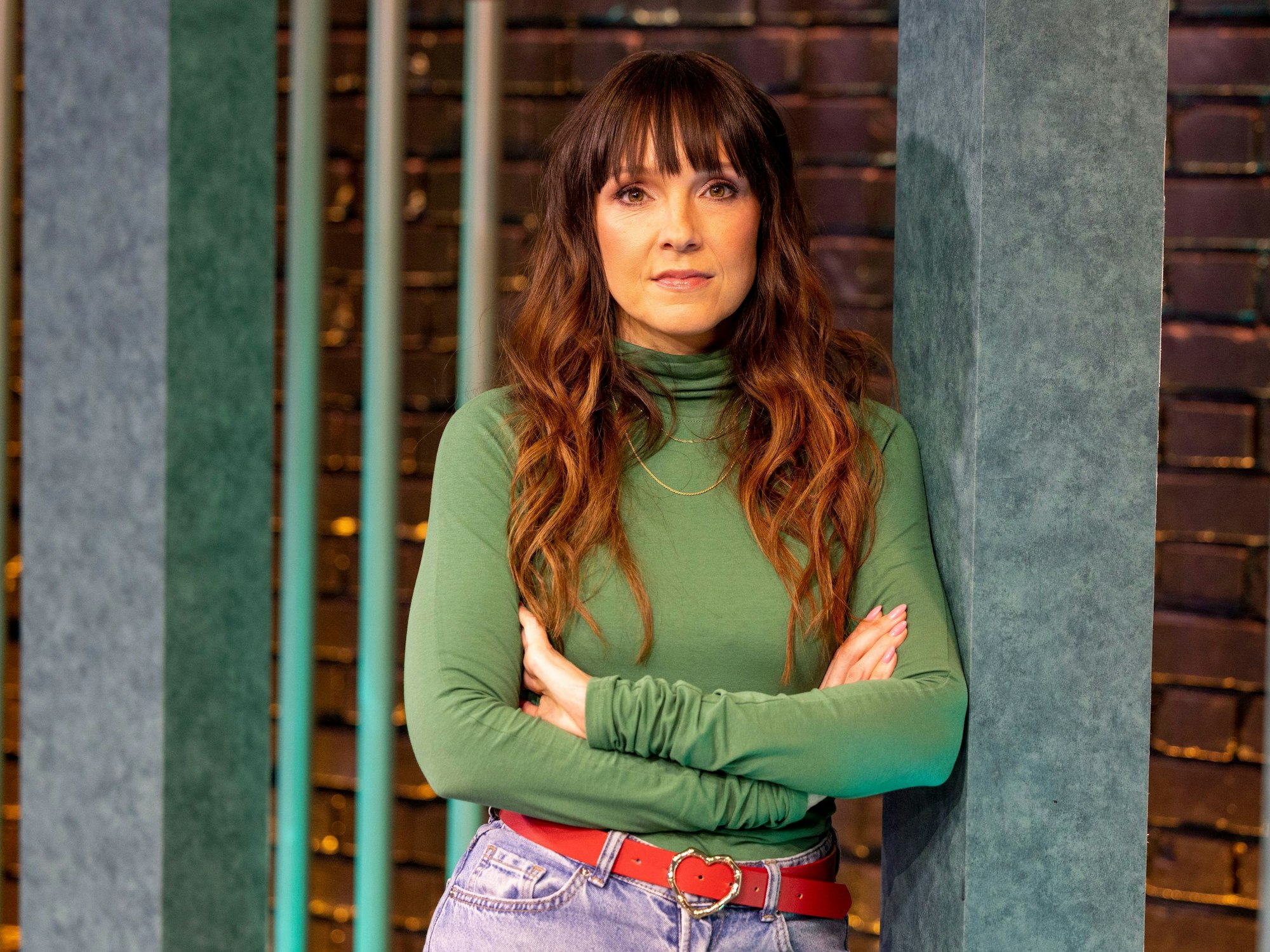 Carolin Kebekus lehnt mit verschränkten Armen an eienr Wand.