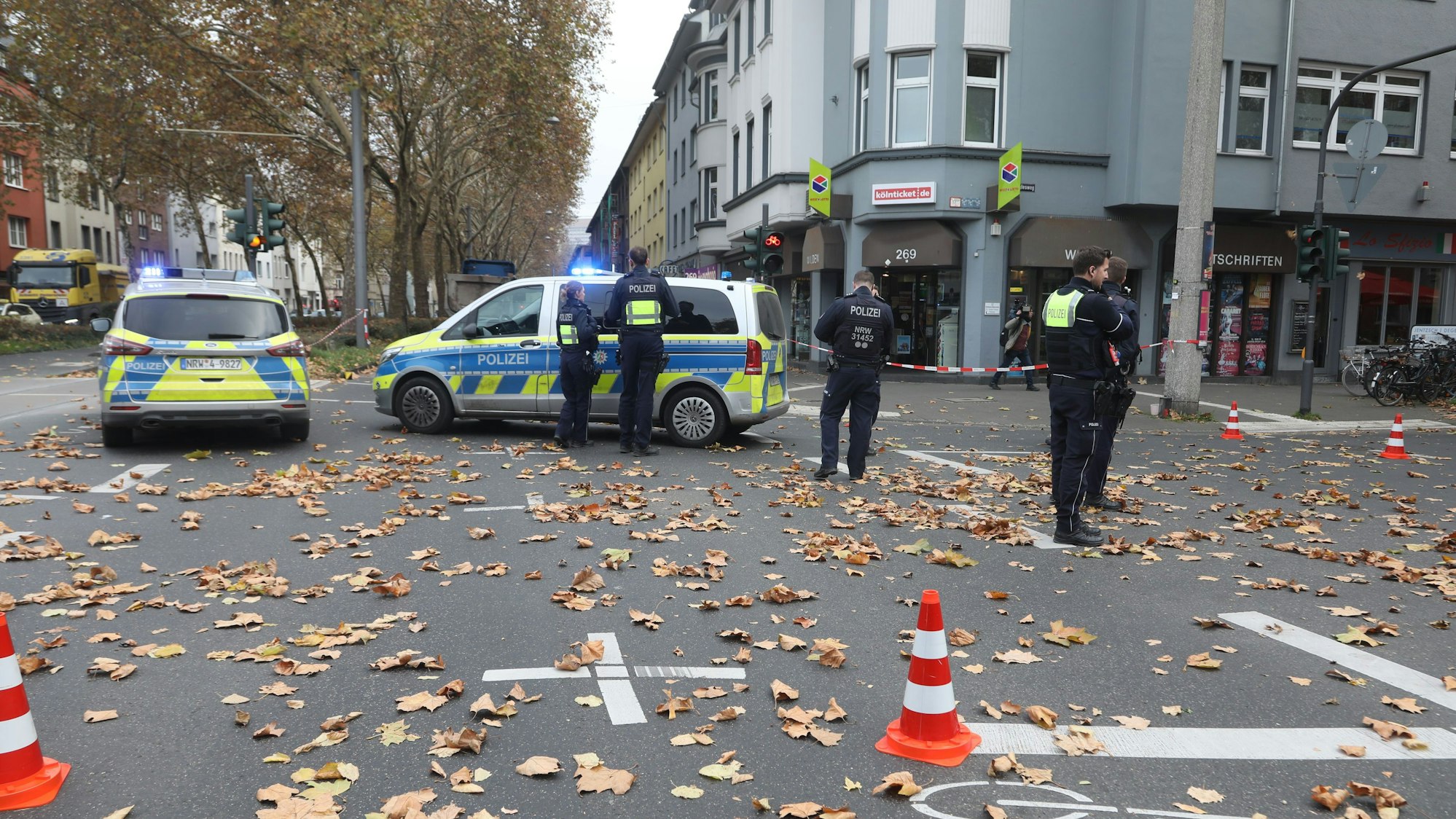 Die Polizei hat eine Kreuzung gesperrt, auf der Fahrbahn stehen mehrere Polizeikräfte und zwei Polizeifahrzeuge.
