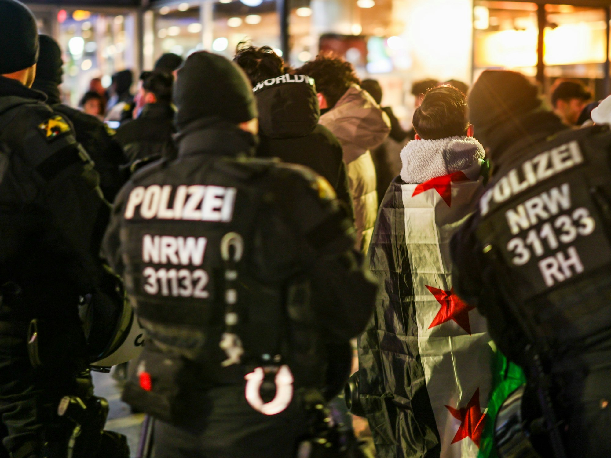 Einsatzkräfte der Polizei sind auf der Straße unterwegs, vor ihnen zahlreiche Menschen.