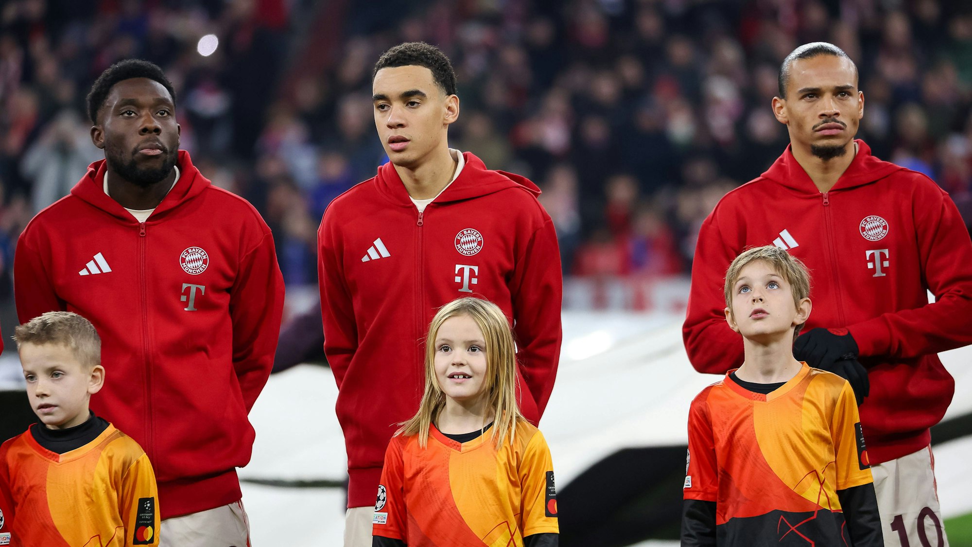 Leroy Sané, Jamal Musiala und Alphonso Davies vor einem Champions-League-Spiel des FC Bayern mit Einlaufkindern.
