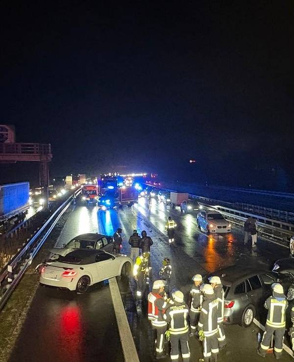Mehrerer Feuerwehrleute stehen nachts auf der Fahrbahn einer Autobahn, vor ihnen mehrere verunfallte Autos.