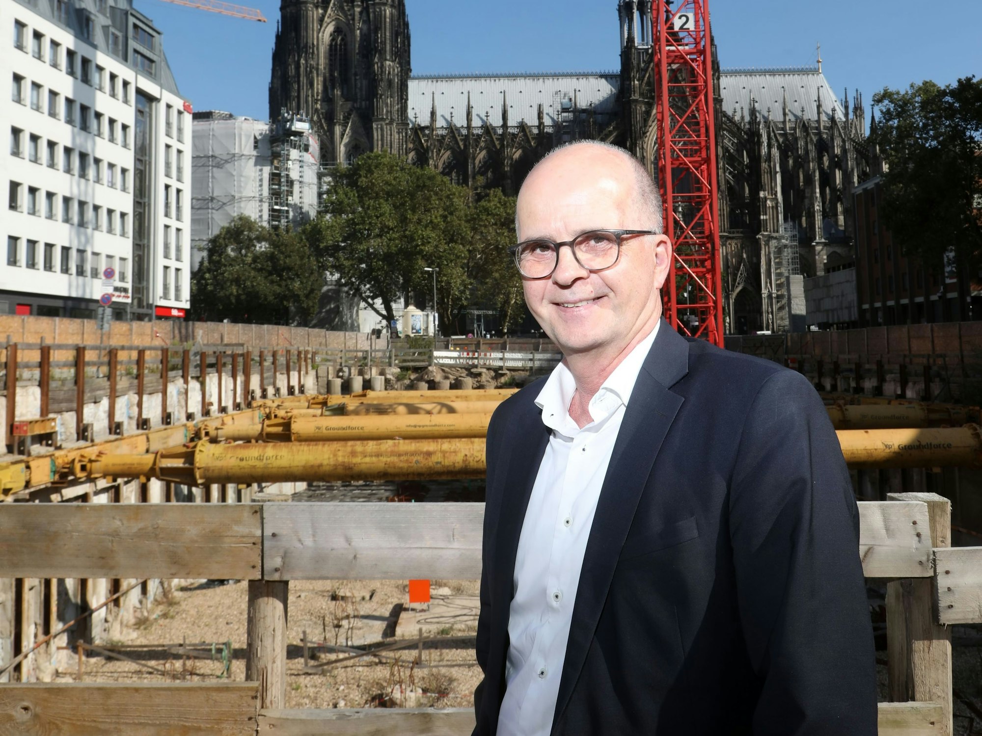 Markus Greitemann steht vor einer großen Baustelle in Köln, im Hintergrund ist der Dom zu sehen.