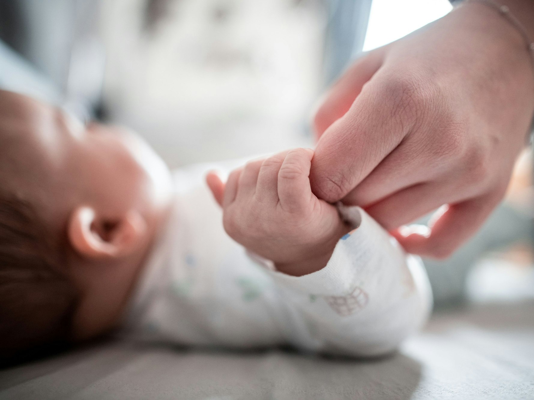 Ein Baby klammert sich an den Finger seiner Mutter.