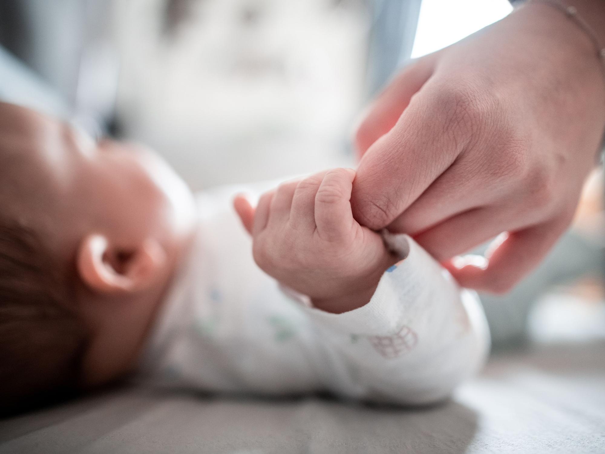 Ein Baby klammert sich an den Finger seiner Mutter.