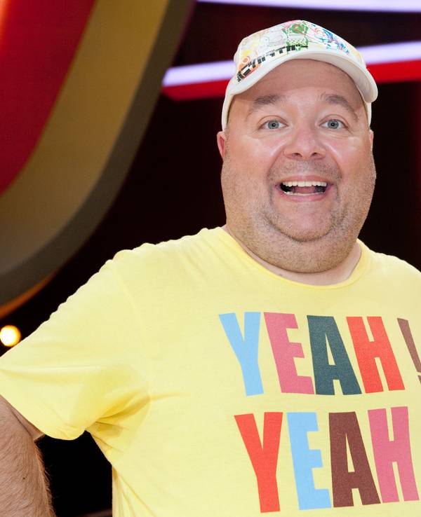 Der Moderator und Entertainer Dirk Bach bei einer Sendung in einem gelben Shirt und mit Mütze.