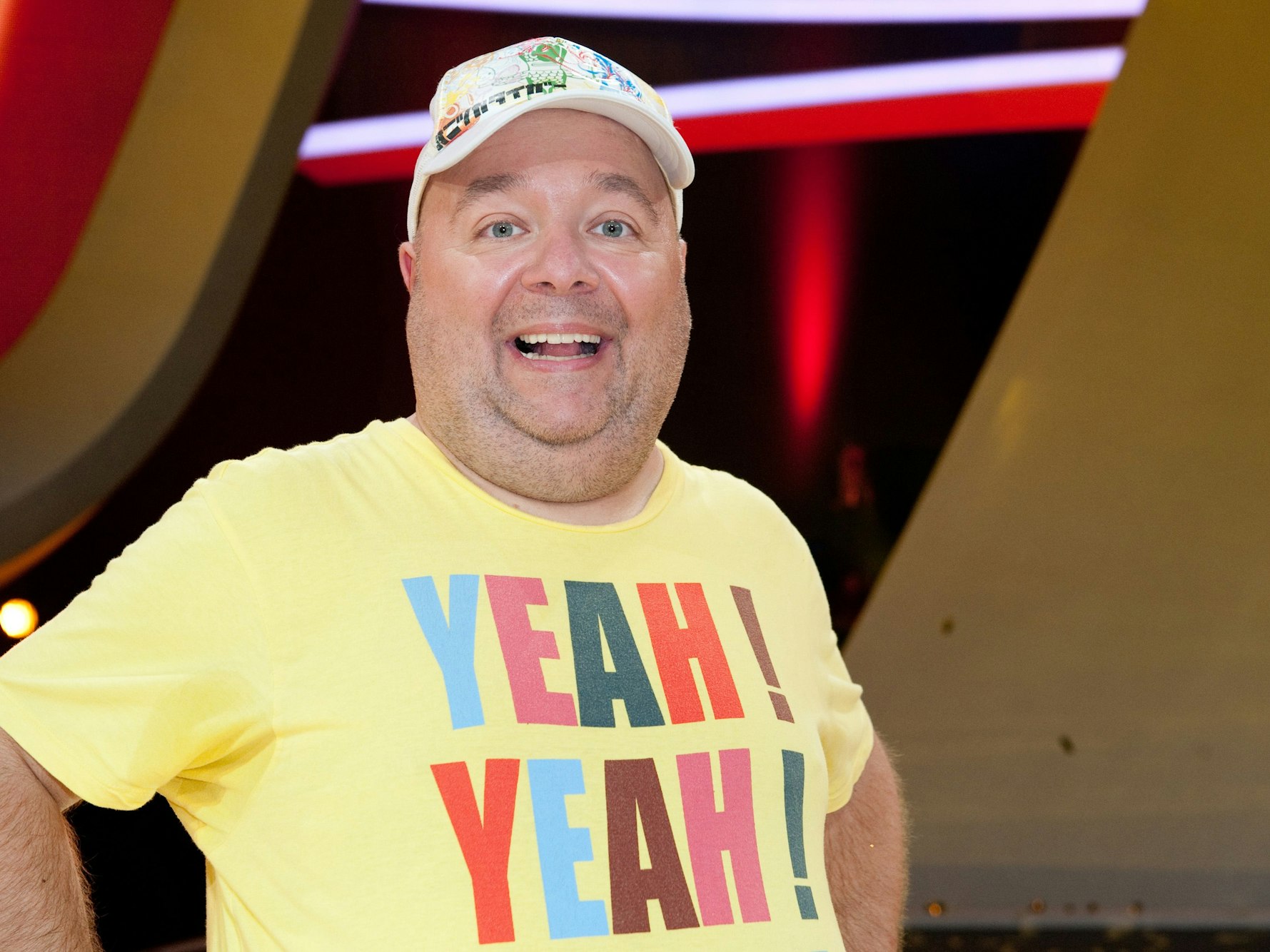 Der Moderator und Entertainer Dirk Bach bei einer Sendung in einem gelben Shirt und mit Mütze.