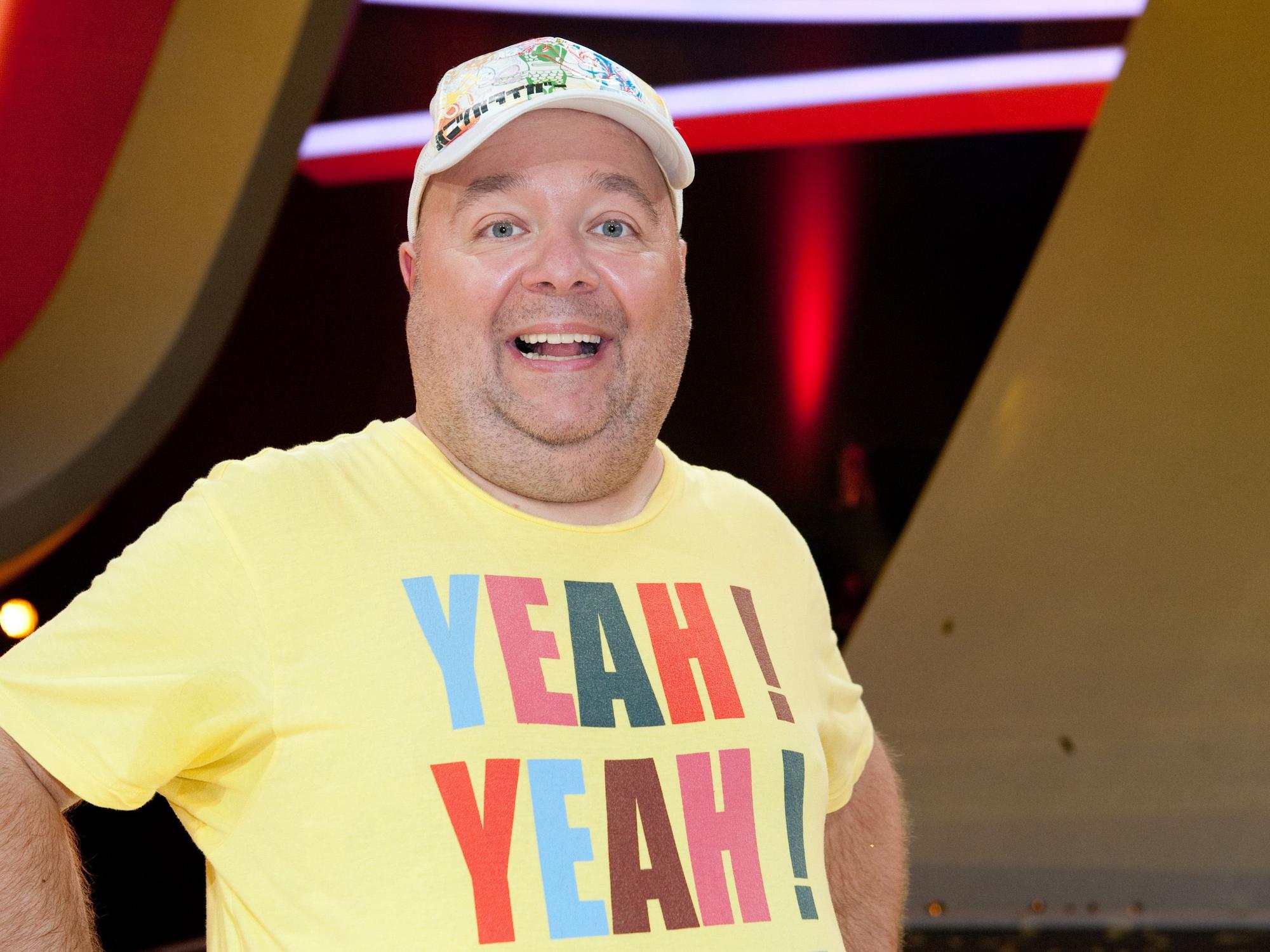 Der Moderator und Entertainer Dirk Bach bei einer Sendung in einem gelben Shirt und mit Mütze.