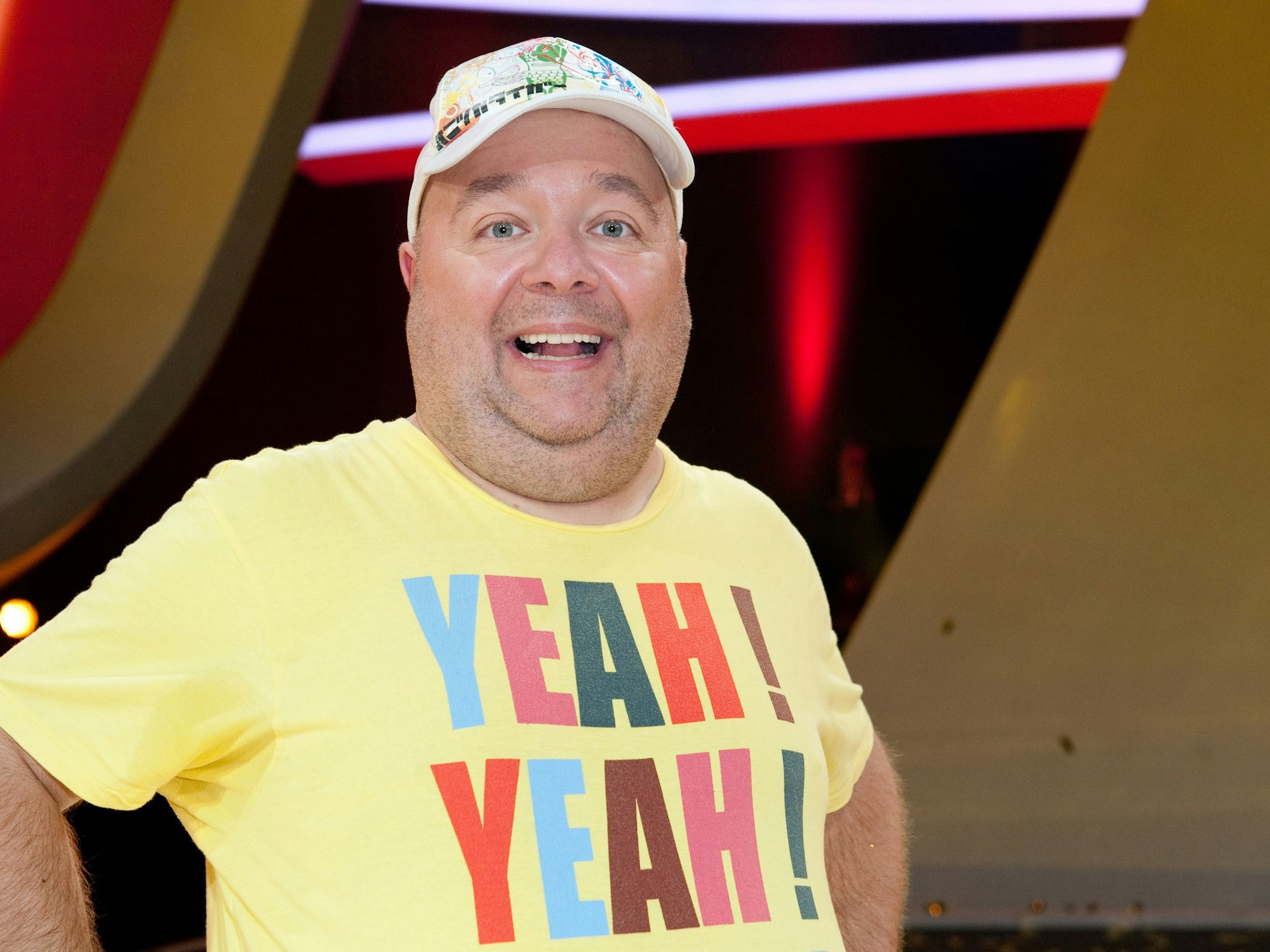 Der Moderator und Entertainer Dirk Bach bei einer Sendung in einem gelben Shirt und mit Mütze.