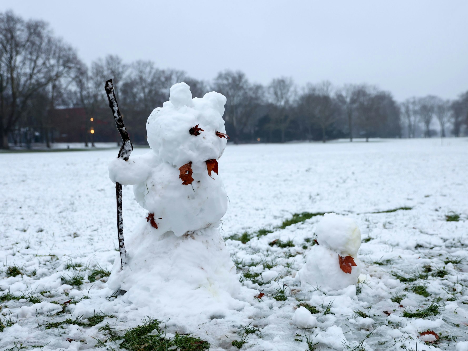 Ein großer und ein kleiner Schneemann stehen auf einer verschneiten Wiese.