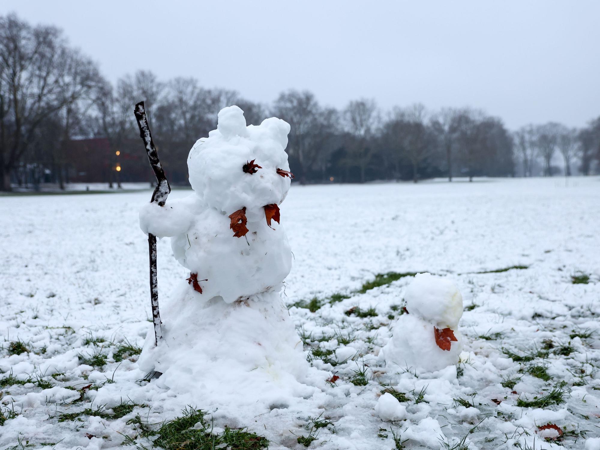 Ein großer und ein kleiner Schneemann stehen auf einer verschneiten Wiese.