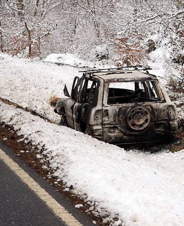 Ein ausgebranntes Fahrzeug steht im Schnee neben einer Straße.