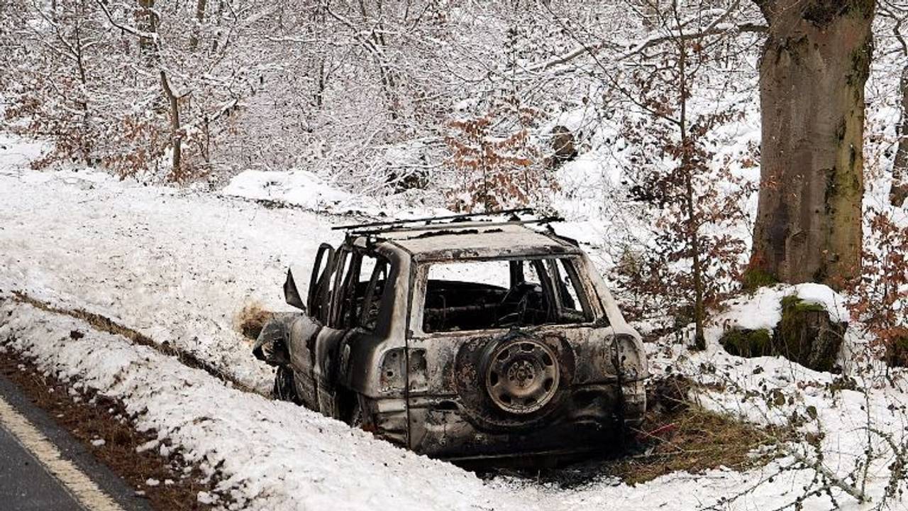 Ein ausgebranntes Fahrzeug steht im Schnee neben einer Straße.