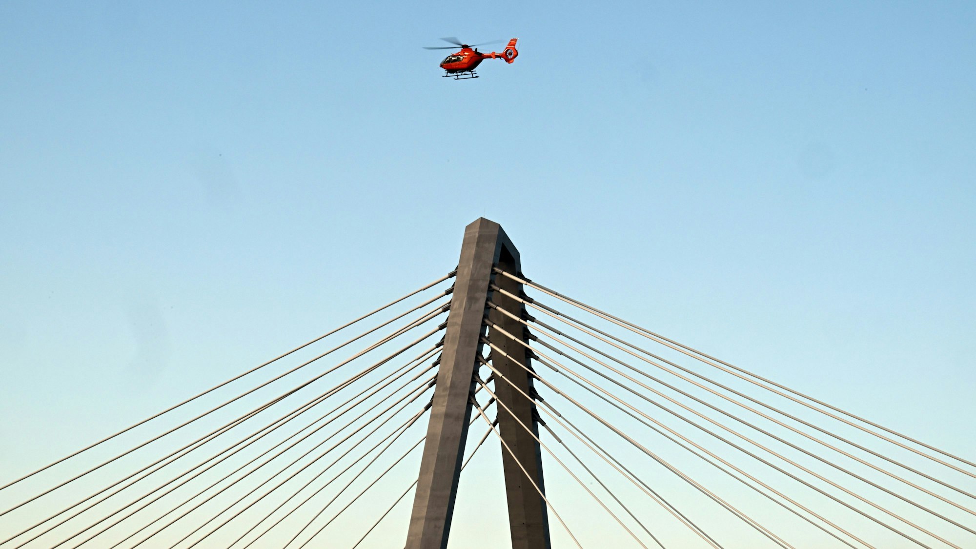 Ein Hubschrauber fliegt über einem Pylonen der Leverkusener Brücke.