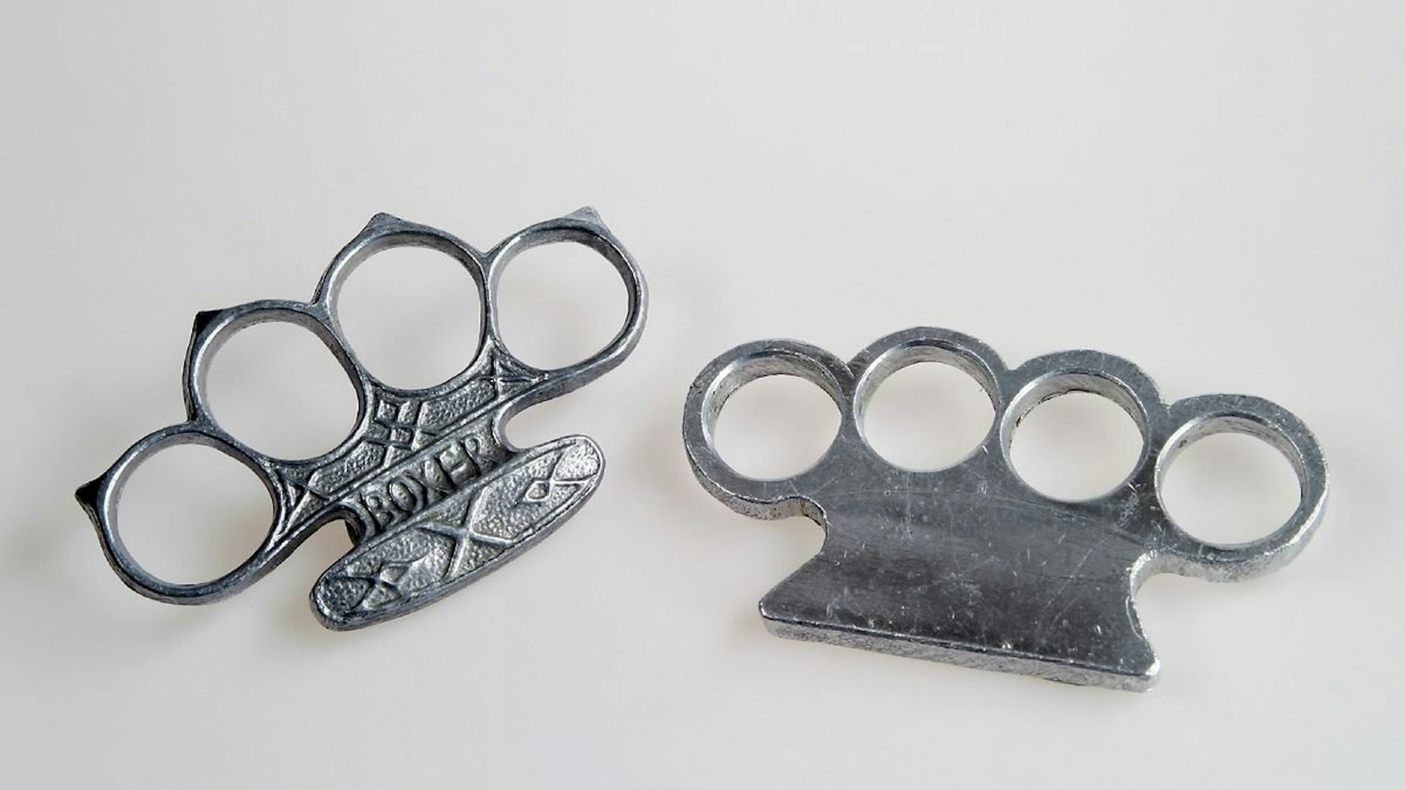 Zwei Schlagringe liegen auf einer einfarbigen Oberfläche.