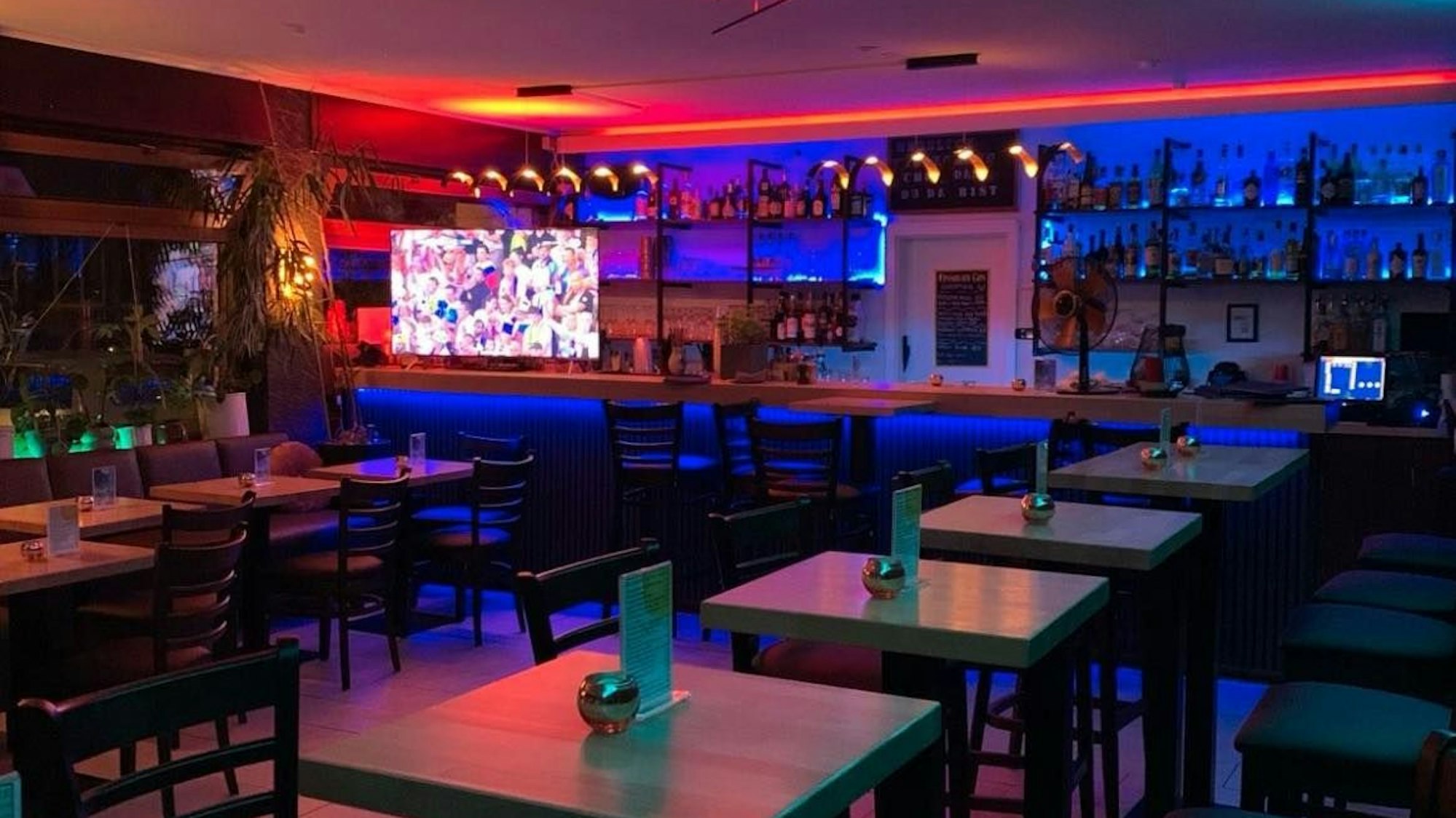 In einem Raum steht eine Bar mit zahlreichen Flaschen, davor mehrere Tische mit Stühlen.