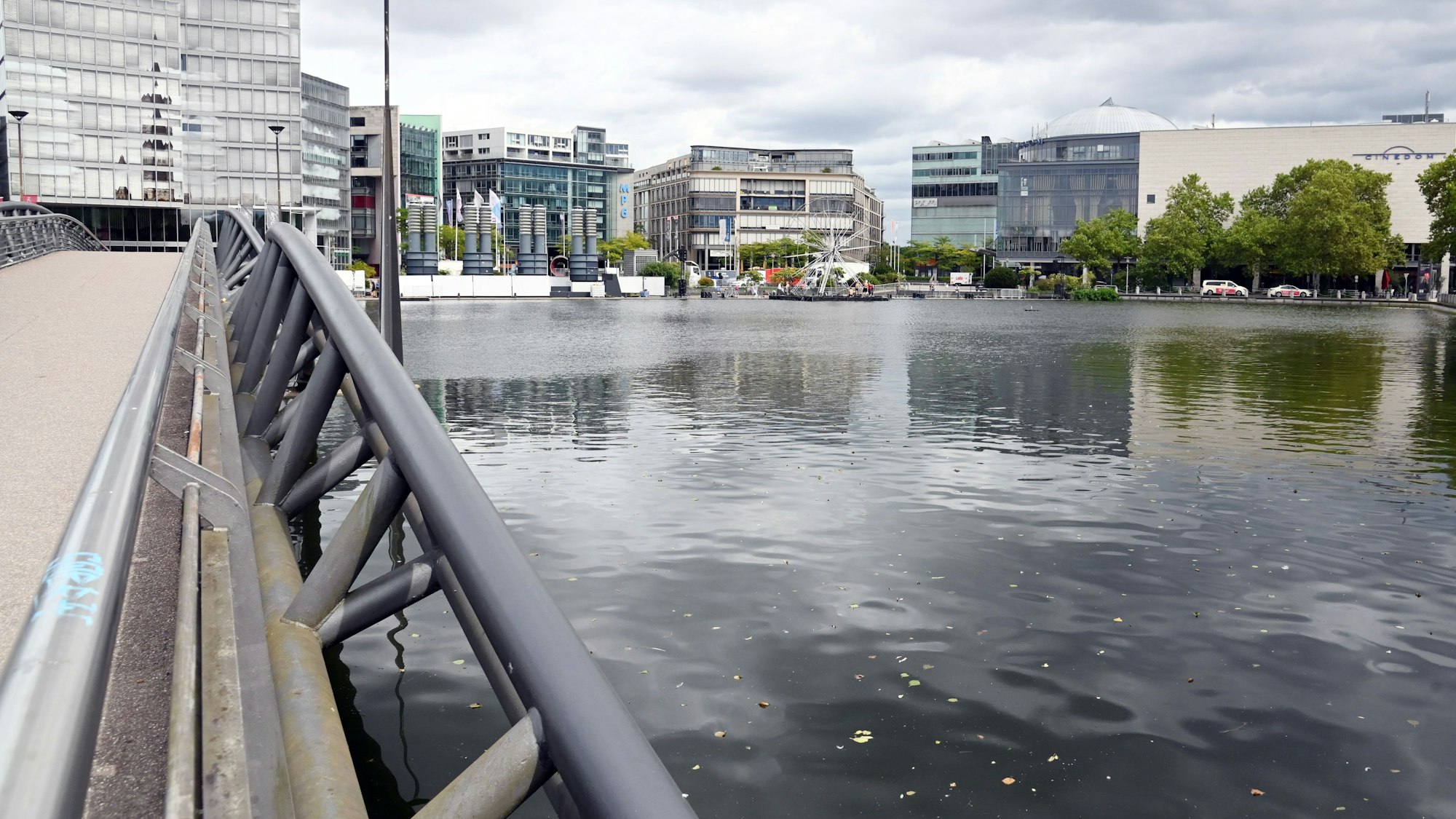An einem Teich führt eine Brücke entlang zu einem Hochhaus.