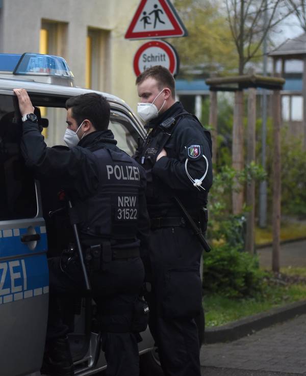 Zwei Polizisten stehen bei einer Razzia an einem Streifenwagen.