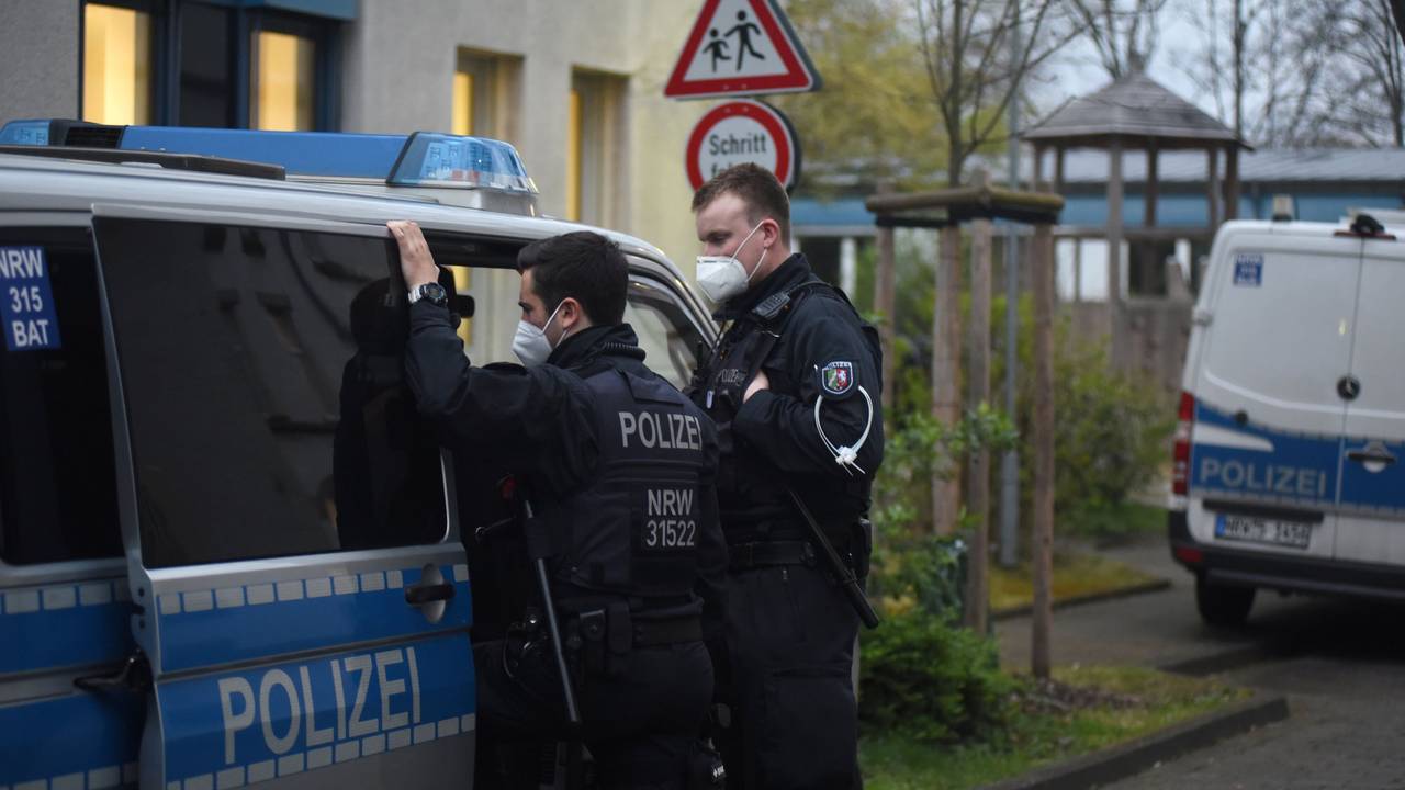 Zwei Polizisten stehen bei einer Razzia an einem Streifenwagen.